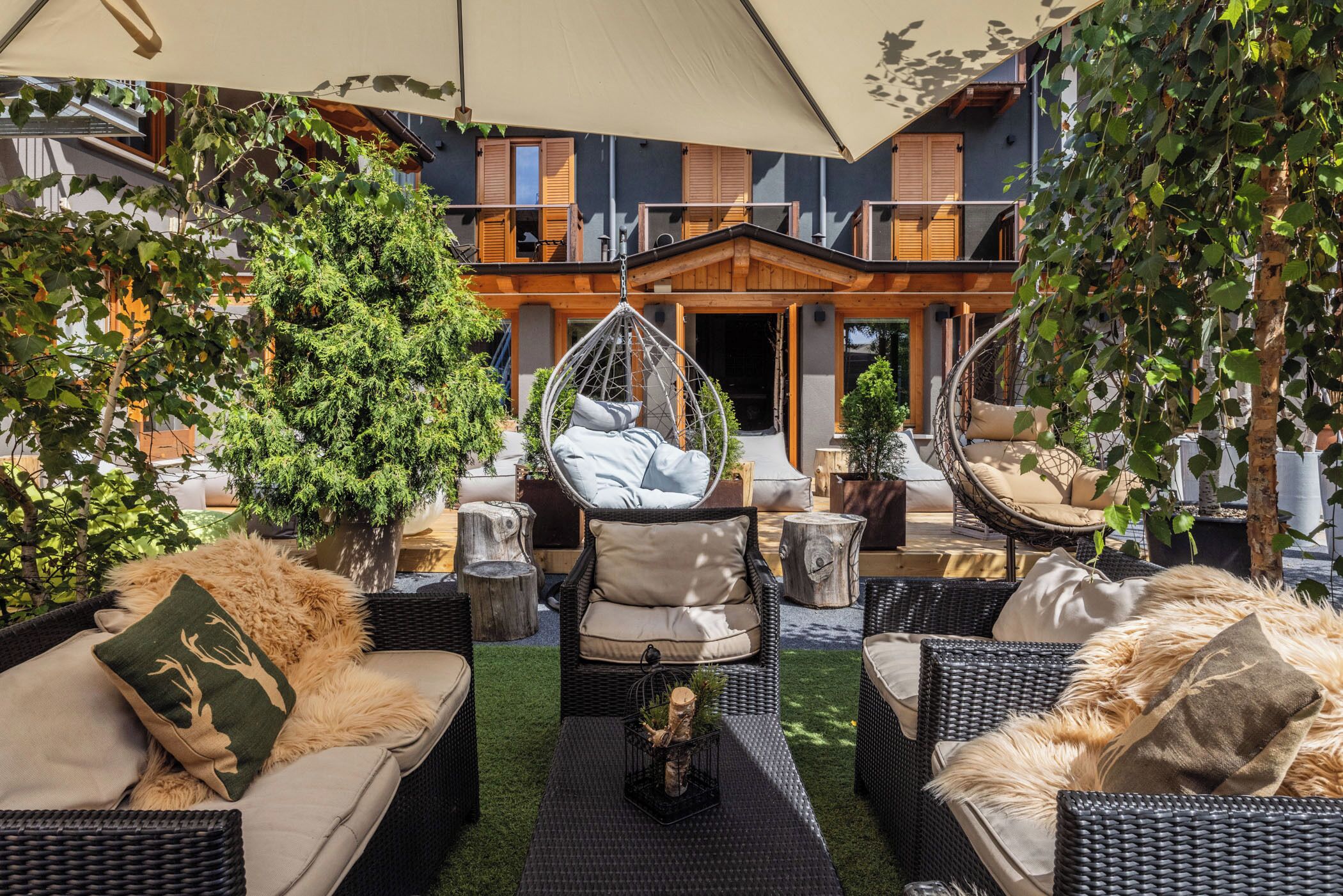 An outdoor seating area with wicker furniture, a hanging chair, and a large umbrella providing shade.