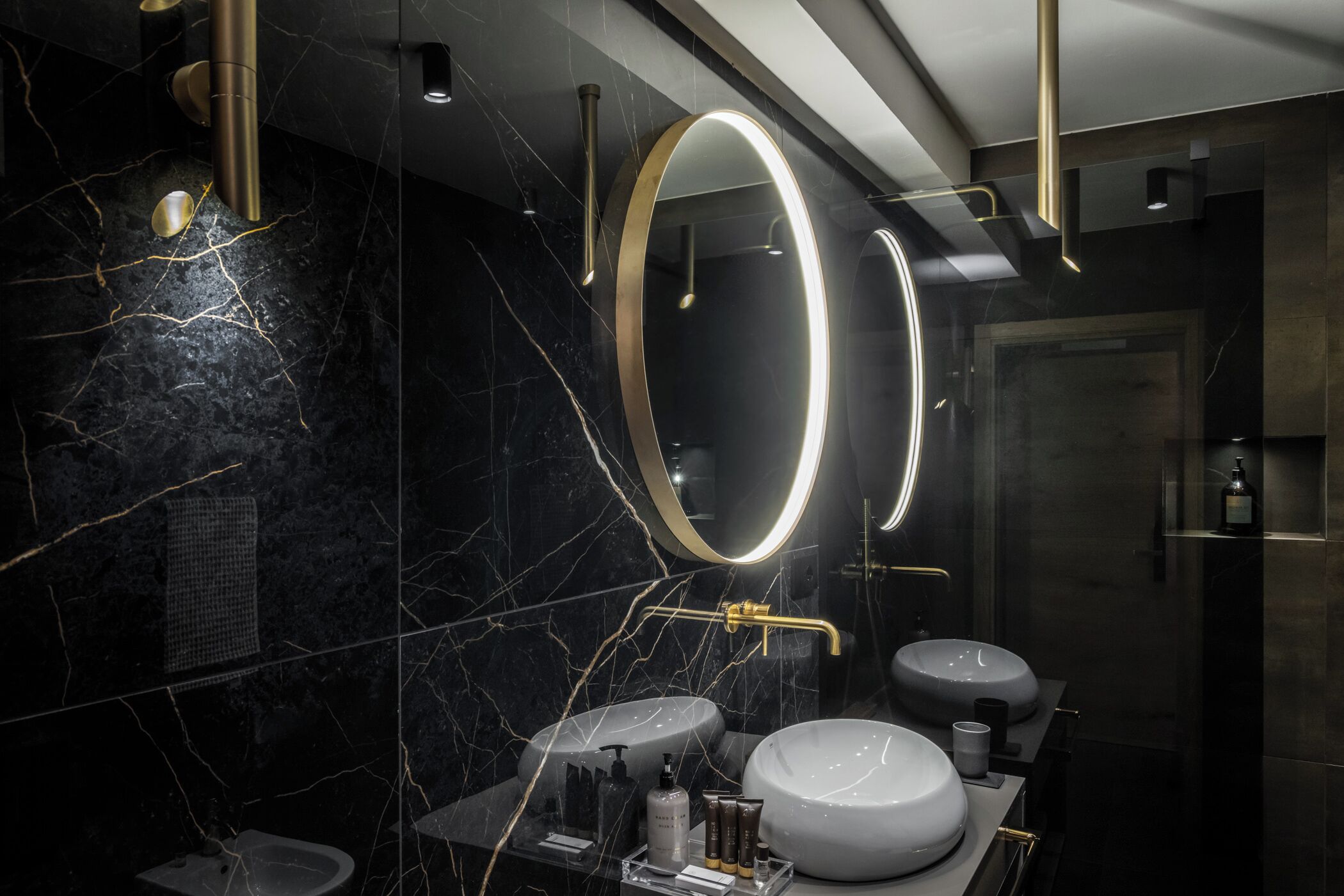 Ein modernes Badezimmer mit Marmorwänden, zwei Waschbecken, einem Bidet und einem Spiegel mit beleuchtetem Rand.