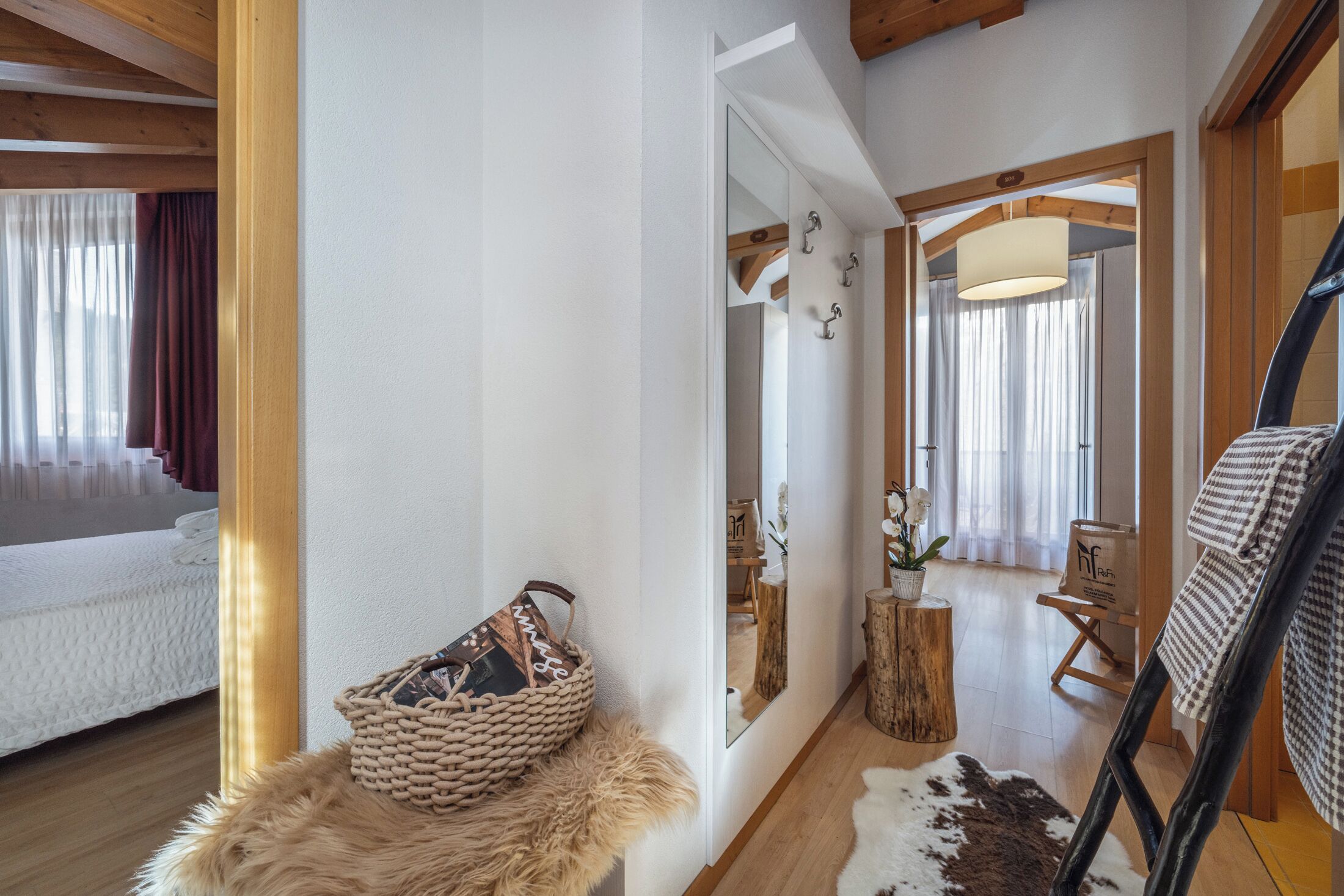 Una habitación con cama, espejo, suelo de madera, alfombra de piel, cesta tejida y taburete de madera.
