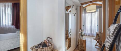 Una habitación con cama, espejo, suelo de madera, alfombra de piel, cesta tejida y taburete de madera.