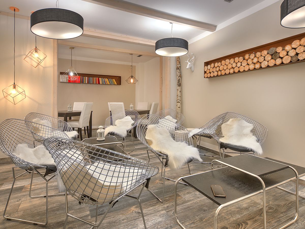 Zona relax moderna con sedie in filo metallico, un tavolo in legno e lampade a sospensione.