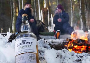 Una botella de whisky Glenlivet Nàdurra en un entorno nevado al aire libre, con una fogata.