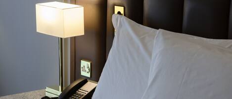 A hotel room with a bed, a bedside lamp, a telephone, and a small picture frame on the nightstand.