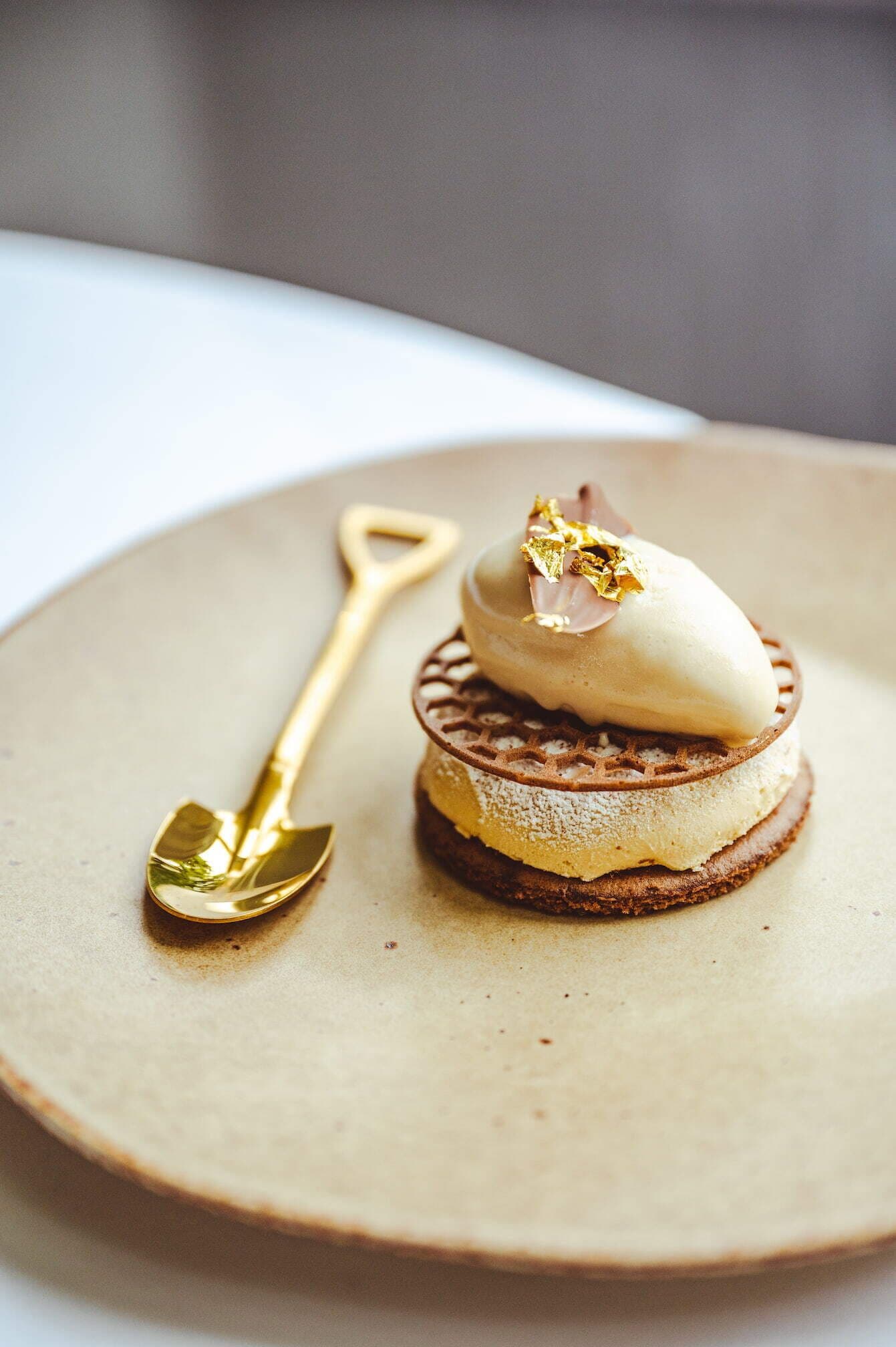 A dessert on a round plate with a golden spoon beside it.