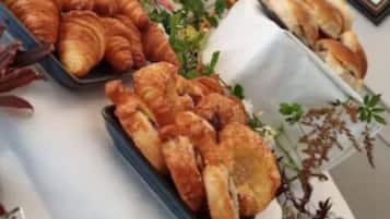 Uma mesa com croissants e outras iguarias, um quadro na parede e um vaso com plantas secas.