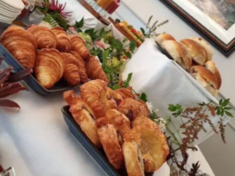 Uma mesa com croissants e outras iguarias, um quadro na parede e um vaso com plantas secas.