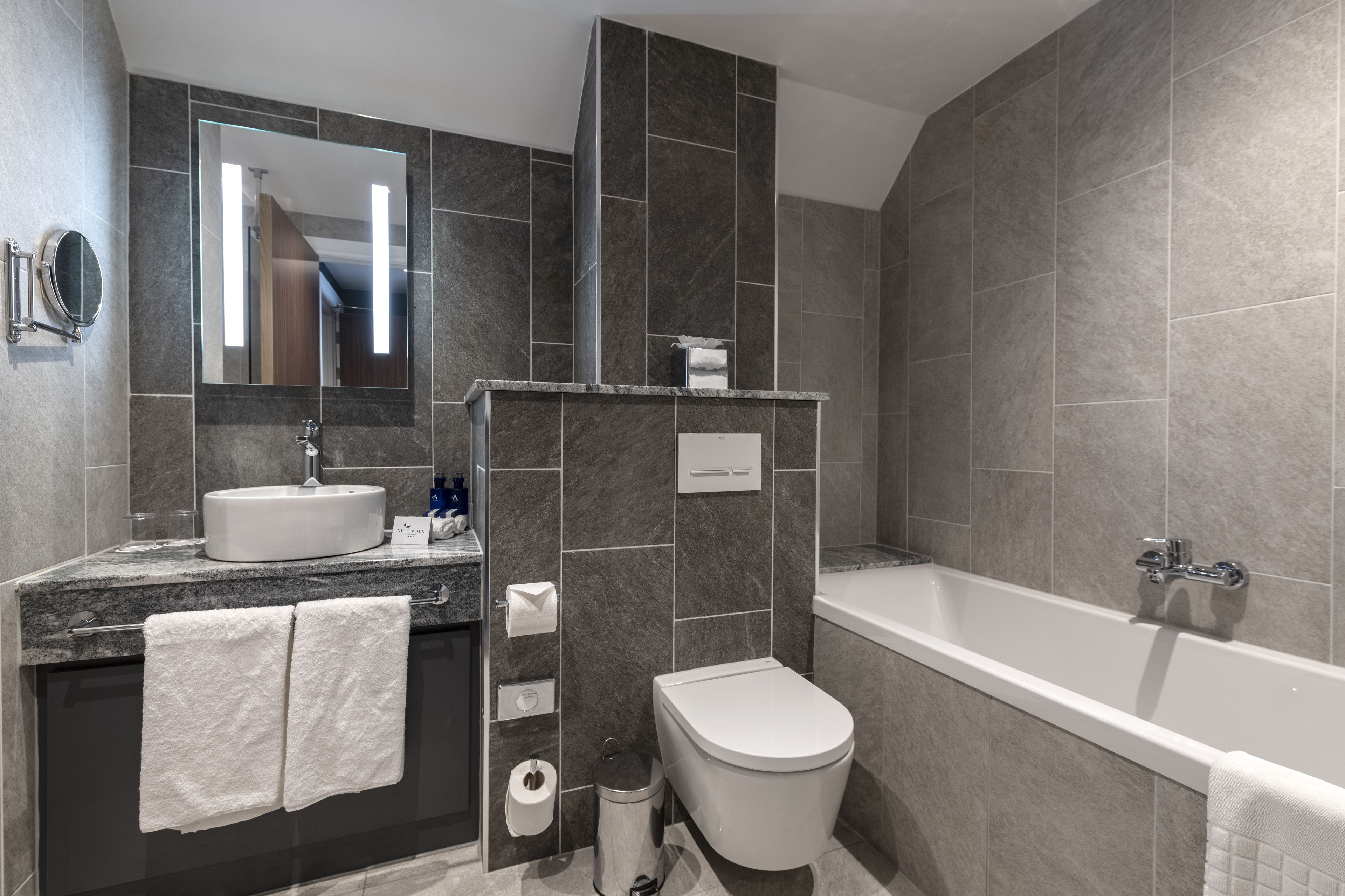Un baño moderno con lavamanos, espejo, inodoro y bañera.