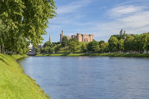 A historic castle on a riverbank with a grassy path and trees.
