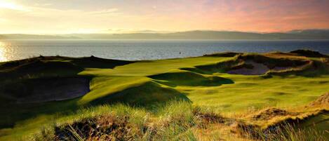 A golf course with a view of the sea and a sunset.