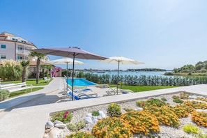 A pool area with umbrellas, a clear view of the sea, and a landscaped garden. - Apartments Fiorido (Medulin)