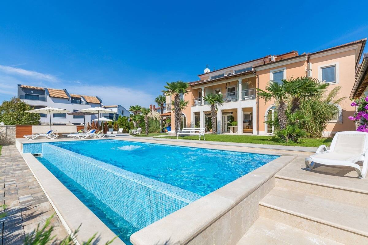 A swimming pool with lounge chairs, a building with balconies, and palm trees.