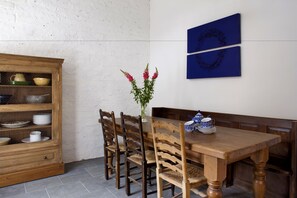 A dining area with a wooden table, chairs, a wooden cabinet with glass doors, and a vase with flowers. - Morton House And Stable Block In Masham (Ripon)