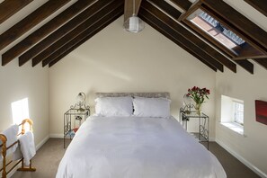A bedroom with a large bed, wooden beams, a skylight, bedside tables, and a window. - Morton House And Stable Block In Masham (Ripon)