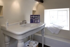 A bathroom with a white sink, a window with a towel, and a basket with toilet paper. - Morton House And Stable Block In Masham (Ripon)