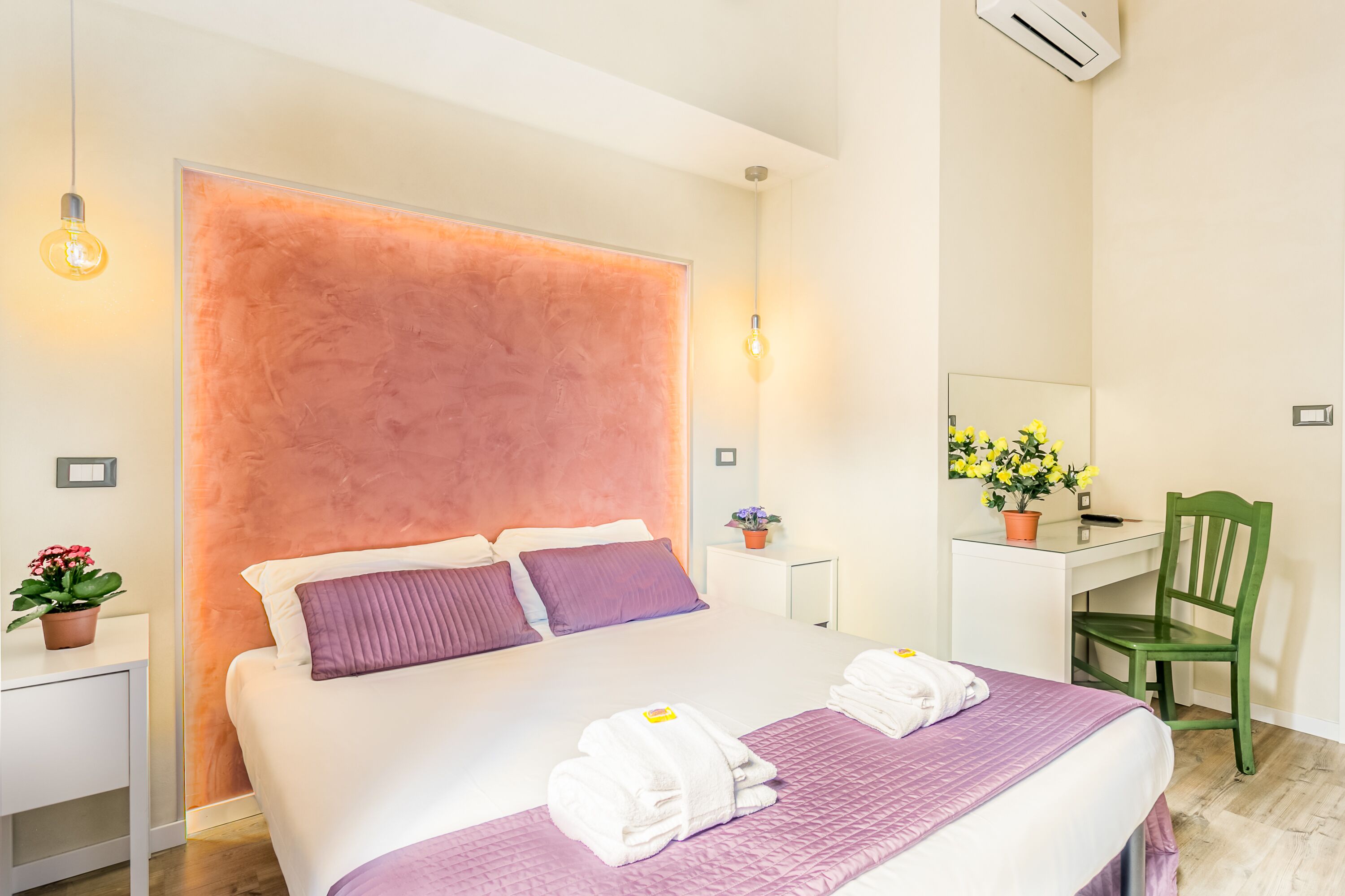 A hotel room with a large bed, a desk, a chair, and a potted plant.