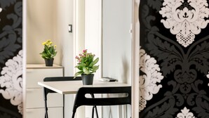 A room with a white desk, two black chairs, a potted plant with yellow flowers, and a potted plant with pink flowers. - AmoRoma Suite (Rome)