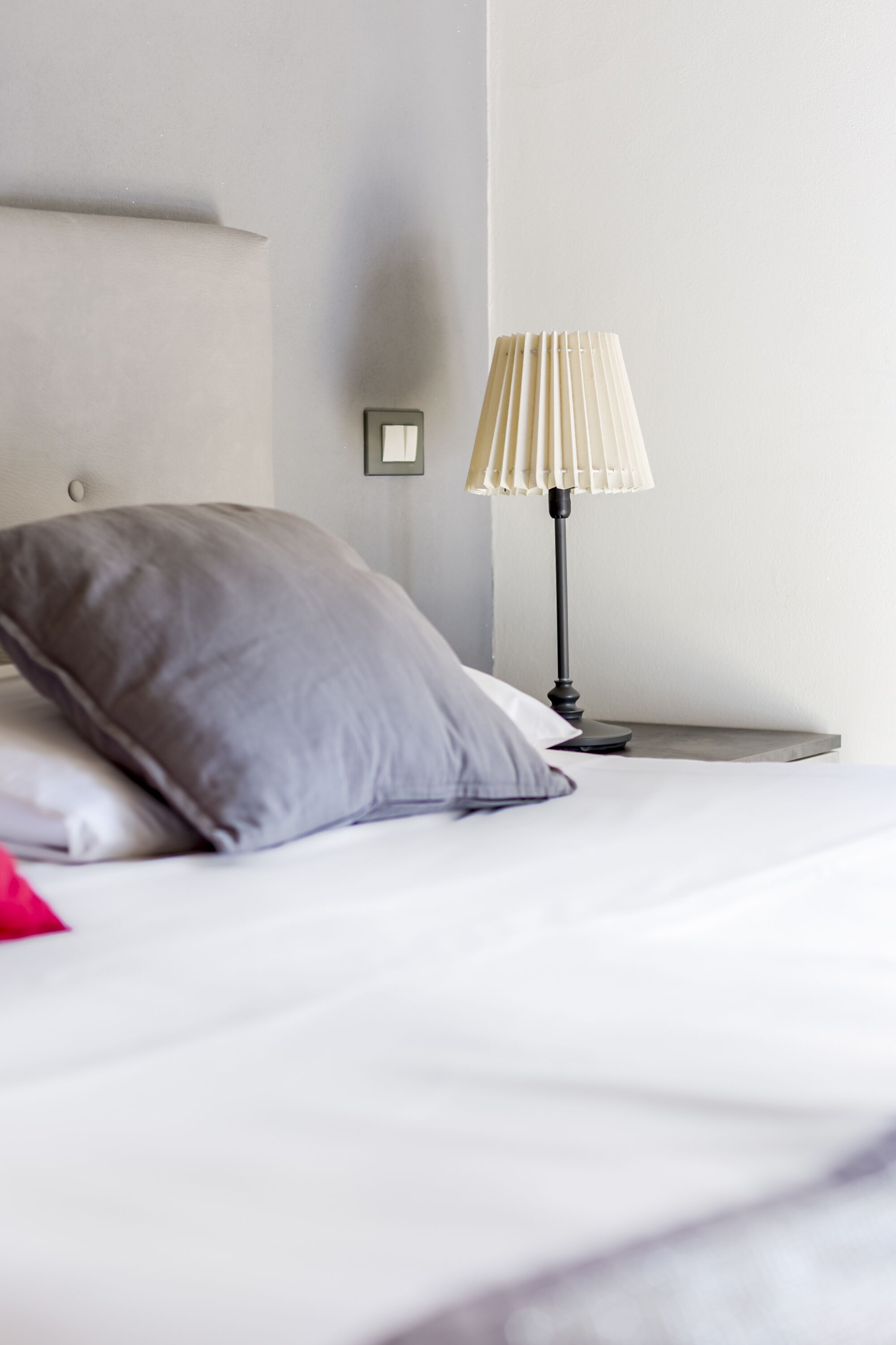 A neatly made bed with a gray pillow, a white pillow, and a small bedside table with a lamp.