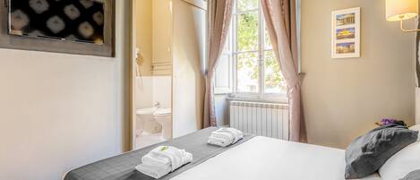 A hotel room with a bed, a TV mounted on the wall, a window with curtains, and a radiator.