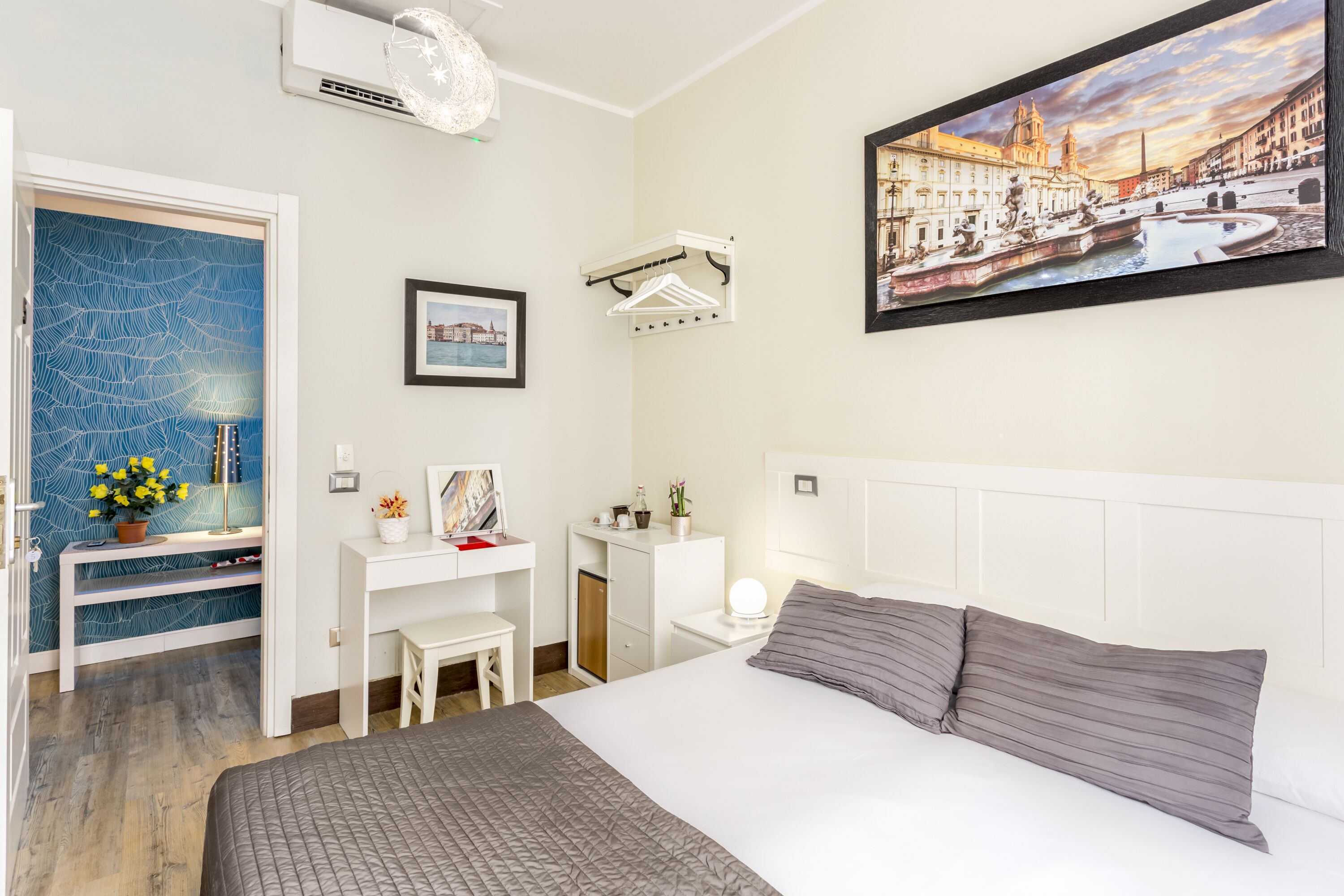 A hotel room with a bed, desk, chair, and a painting of a cityscape.