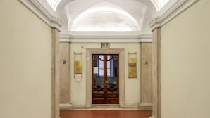 A hallway with a high ceiling, columns, and a door at the end. - AmoRoma Suite (Rome)