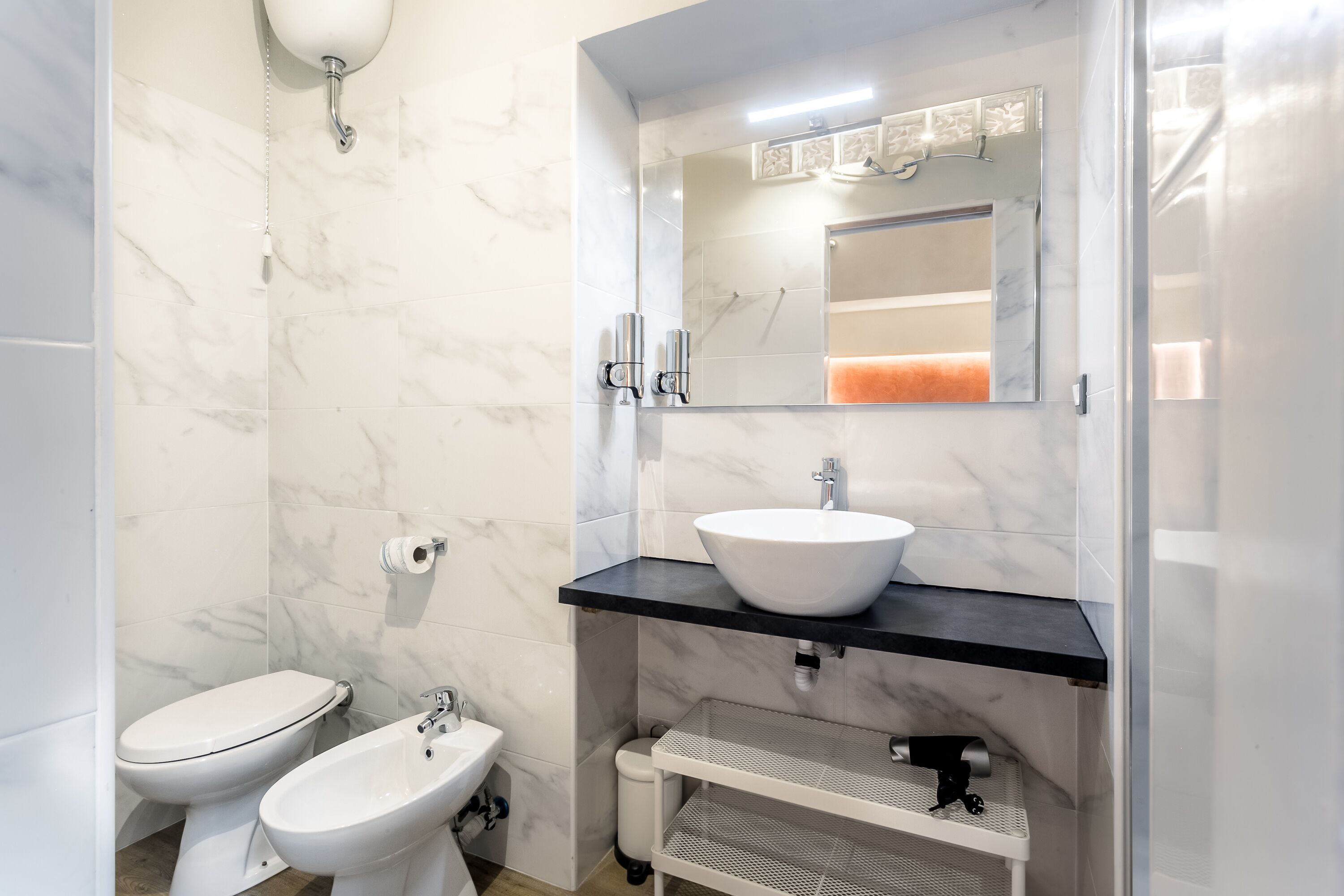 A bathroom with a white toilet, bidet, and a sink with a mirror above.