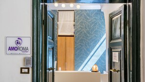 A hotel entrance with a sign for the Amoroma suite, a wooden cabinet, and a towel hanging on the wall. - AmoRoma Suite (Rome)