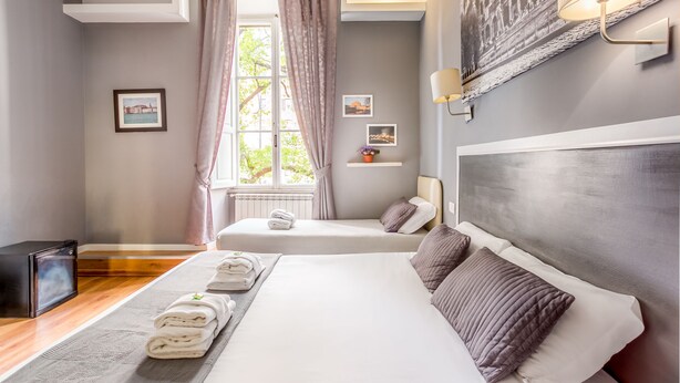 A hotel room with a large bed, a smaller bed, a TV, a window with curtains, and wall-mounted artwork. - AmoRoma Suite (Rome)