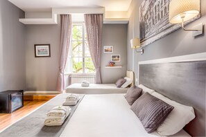 Habitación de hotel con una cama grande, una cama más pequeña, un televisor, una ventana con cortinas y una obra de arte colgada en la pared.