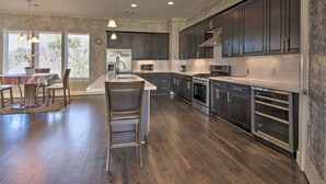 A modern kitchen with dark cabinets, a central island, and a dining area with a table and chairs. - Brand New 3 Story Modern Home (Houston)