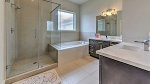 A modern bathroom with a glass-enclosed shower, a freestanding bathtub, and a vanity with a large mirror. - Brand New 3 Story Modern Home (Houston)