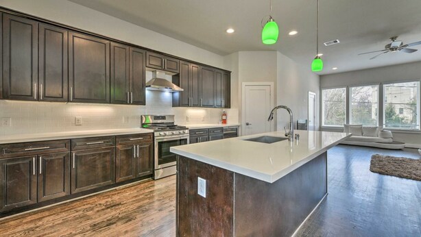 A modern kitchen with dark wood cabinets, a large island, and a ceiling fan. - Brand New 3 Story Modern Home (Houston)
