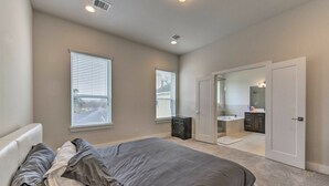 A bedroom with a large bed, a dresser, and a walk-in closet leading to a bathroom. - Brand New 3 Story Modern Home (Houston)