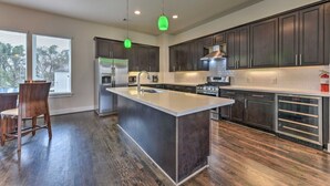 A modern kitchen with dark cabinets, a central island, stainless steel appliances, and pendant lighting. - Brand New 3 Story Modern Home (Houston)