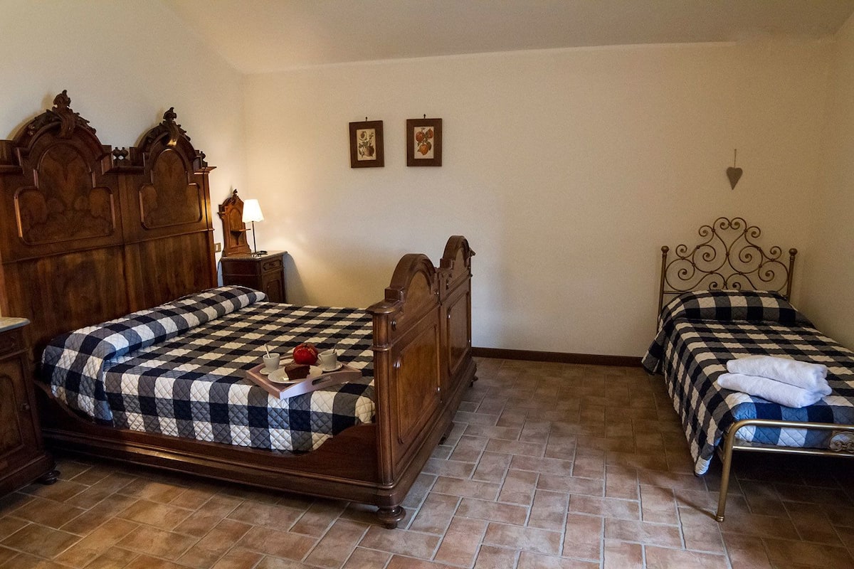 A room with two beds, a wooden headboard, a nightstand with a lamp, and a small table with a tray of breakfast items.