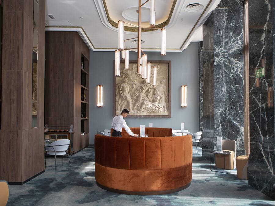 A lobby with a central orange reception desk, marble walls, and a large artwork above the desk.