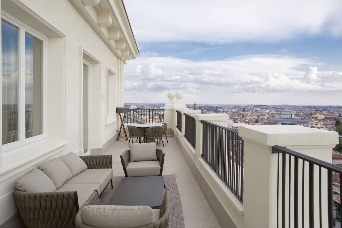 A balcony with a sofa, chairs, and a table, overlooking a cityscape.