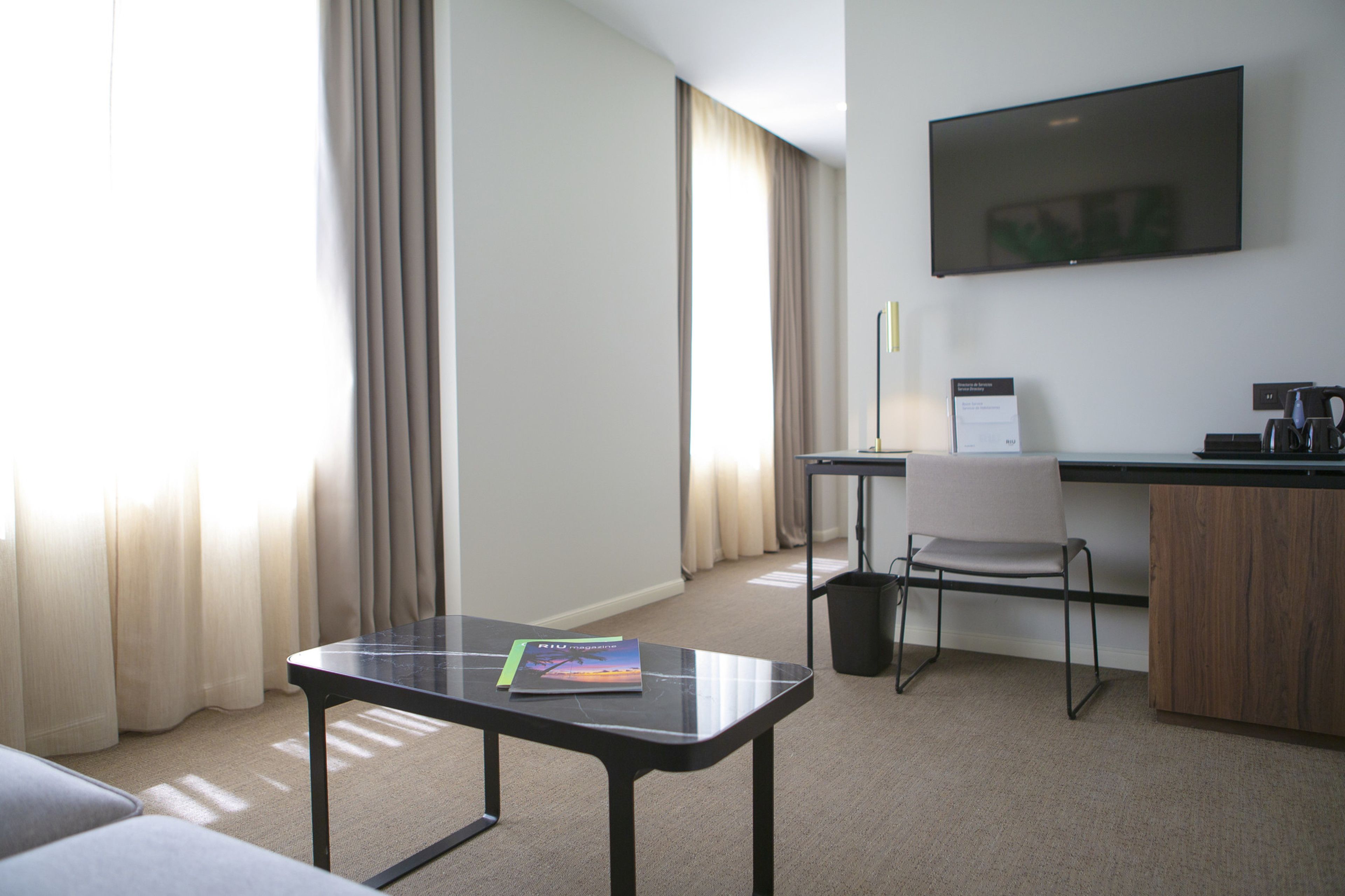 A hotel room with a desk, chair, and a flat-screen TV on the wall.