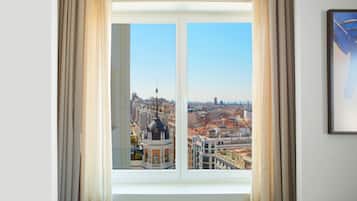 A room with a large window offering a cityscape view, curtains, and a framed picture on the wall.
