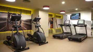 Un gimnasio con cintas de correr, elípticas y una pantalla de televisión.