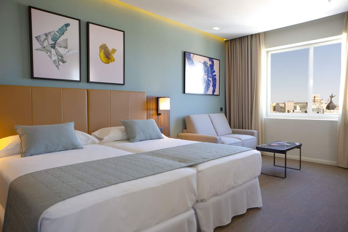 A hotel room with two beds, a sofa, a small table, and artwork on the walls.
