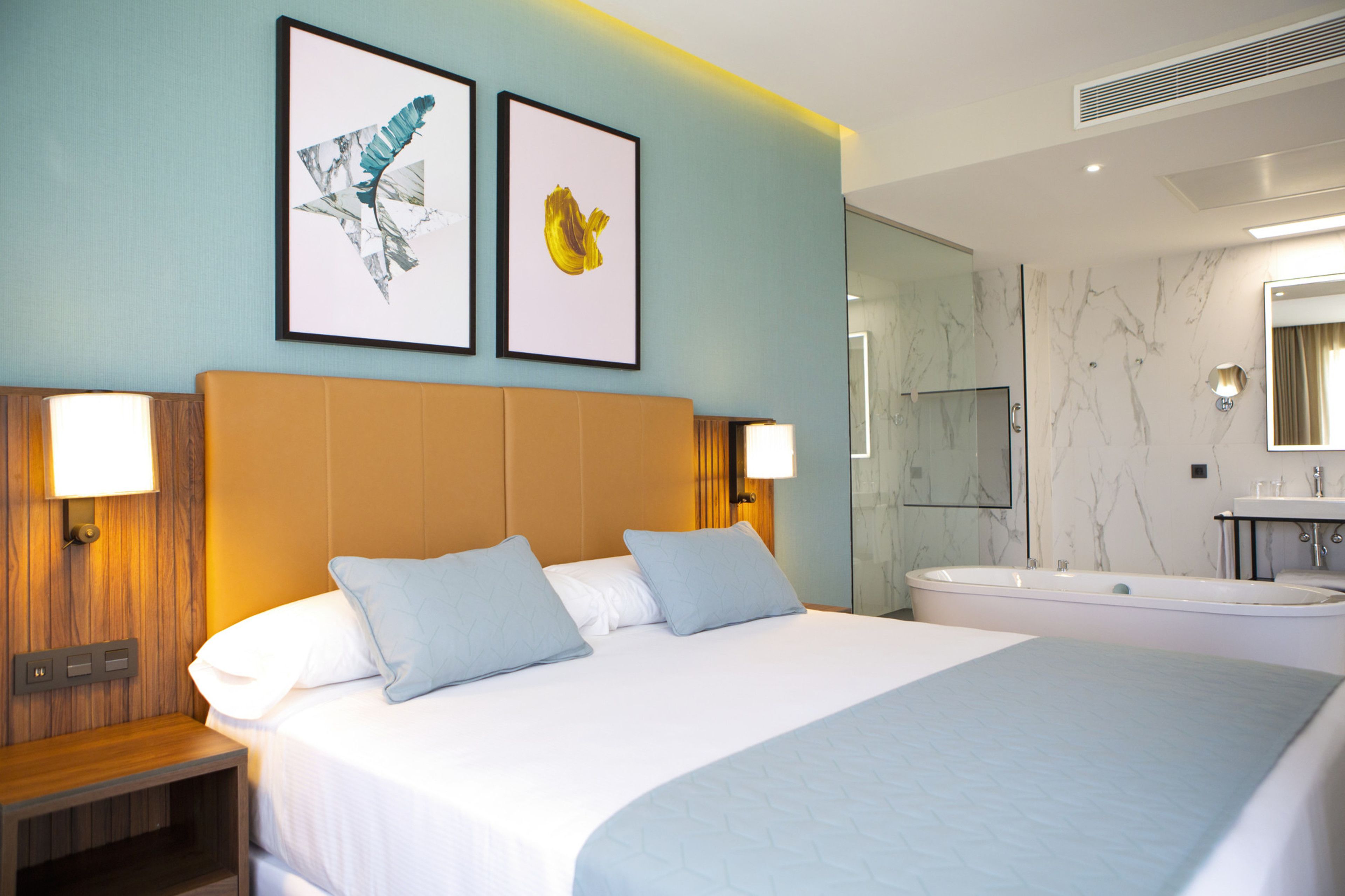 Une chambre d’hôtel avec un grand lit, deux lampes fixées au mur, une baignoire et un mur en marbre.