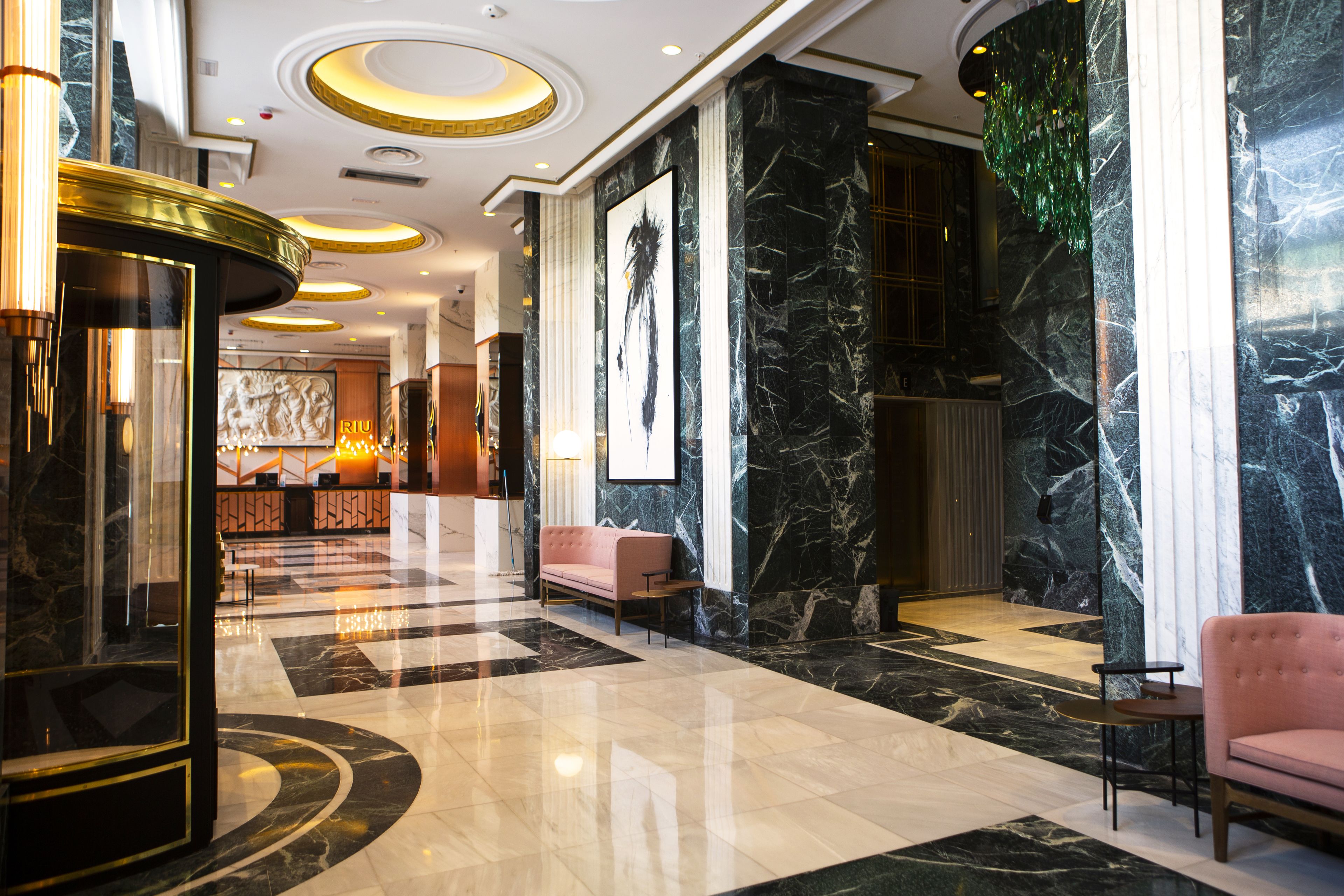 A spacious lobby with a marble floor, a reception desk, a pink sofa, and a large framed artwork on the wall.