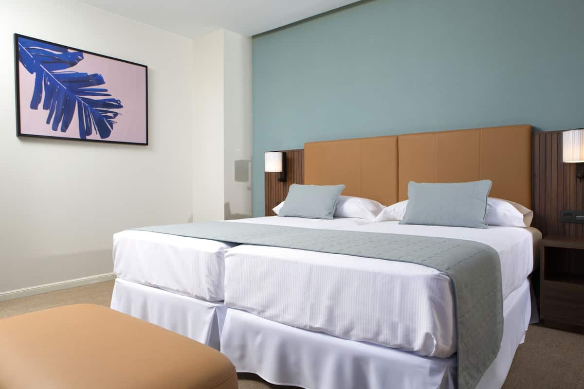 A hotel room with a large bed, two pillows, a nightstand with a lamp, and a framed picture on the wall.