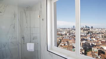 Un baño con mampara de vidrio y ventana con vista a la ciudad.