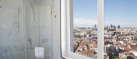 A bathroom with a glass shower door and a window overlooking a cityscape.