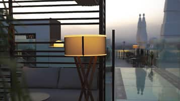 A modern lounge area with a sofa and a table, a lamp, and a view of a building through a glass wall.