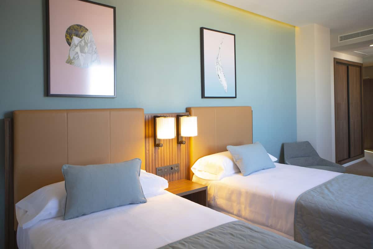 A hotel room with two beds, a nightstand, and two wall-mounted lamps.