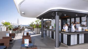 Eine Außenbar mit Sitzgelegenheiten und einer Theke, gestaltet im modernen Stil und mit Blick auf die Stadt.