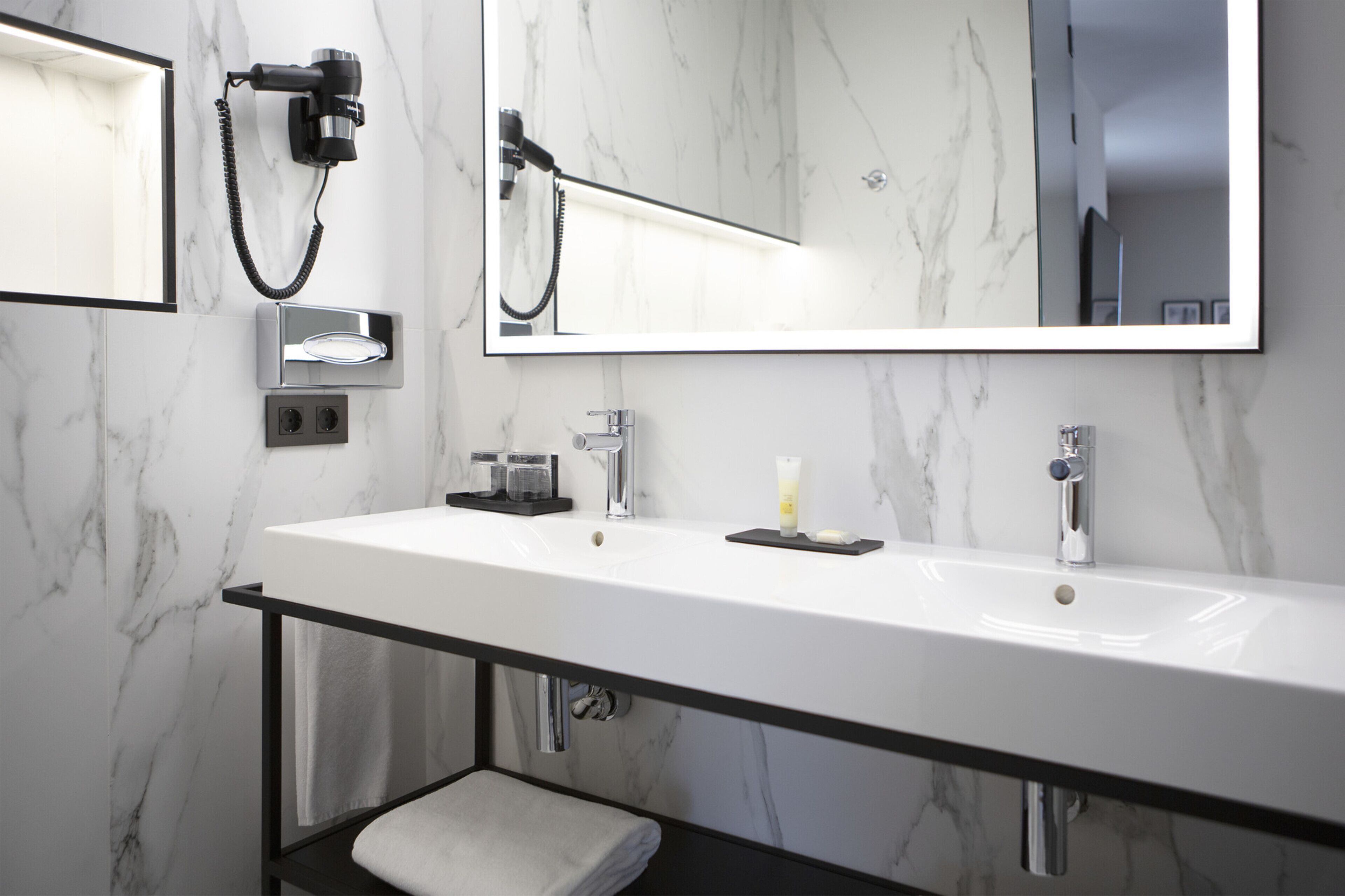 A modern bathroom with a large mirror, a white sink, and a towel rack.