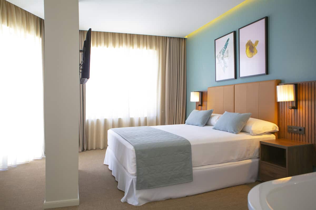 A hotel room with a large bed, a bedside table, a lamp, and a wall-mounted TV.